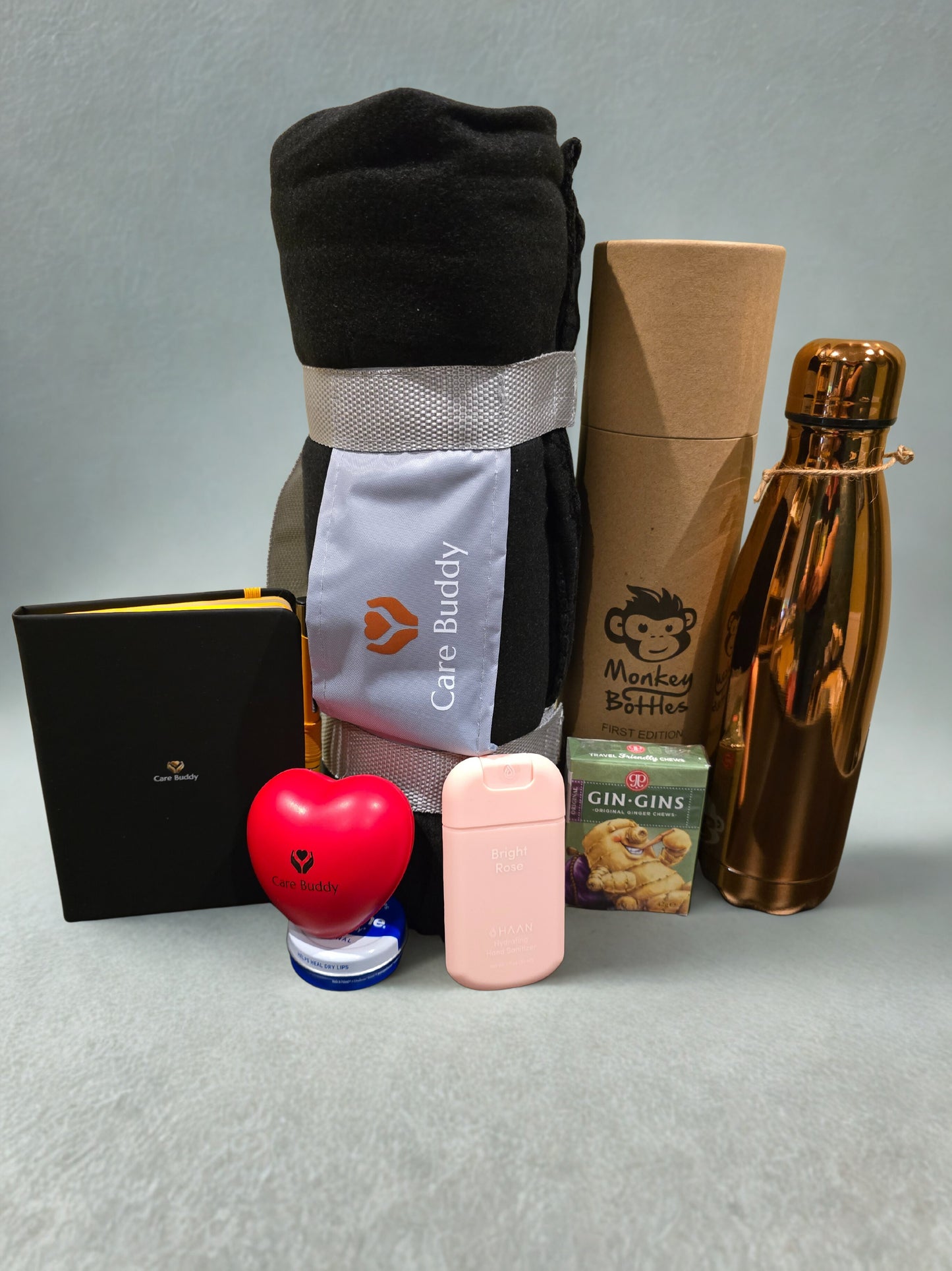 Essential Chemo Package for Hier containing cosy Fleece black blanket that rolls up into a holder, Monkey Bottle colour Rose Gold keeps drinks Cold 24hrs and Warm for 12hrs. Black Journal and Yellow Pen. Red Heart shaped Stress Ball. Gin Gin chews for Nausea. Vaseline Lip Balm. Haan Hydrating spray Hand Sanitizer