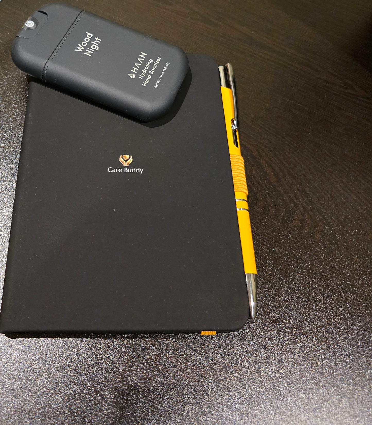 Black Journal with a yellow pen and black Wood Night Hydrating Hand Sanitizer spray