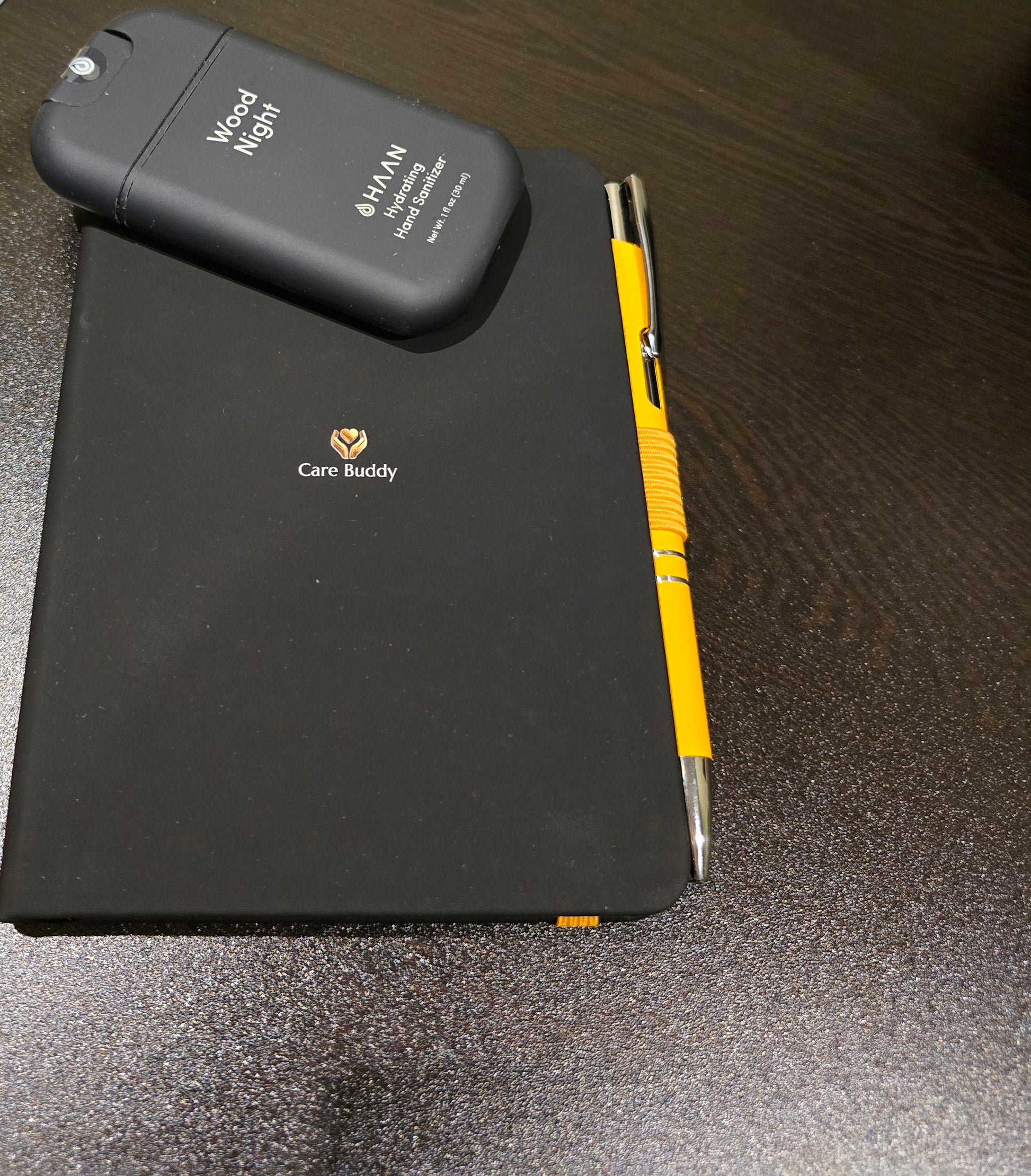 Black Journal with a yellow pen and black Wood Night Hydrating Hand Sanitizer spray