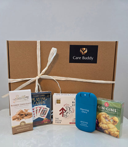 Care Buddy gift box with assorted items including chocolate, playing cards, Black Stuff Body Soap, Hydrating Hand Sanitizer and Gin Gis Ginger Chews