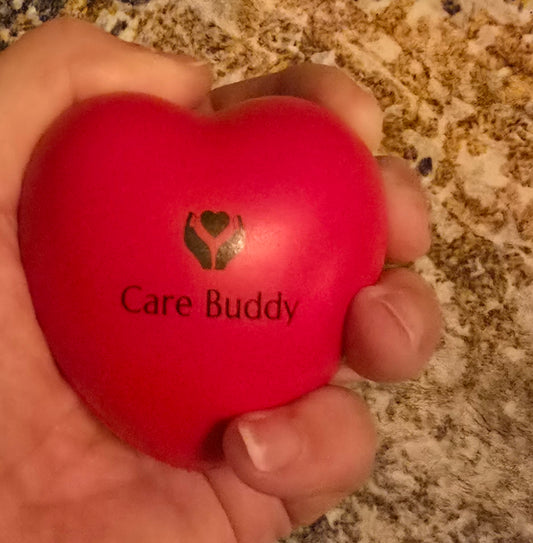 Red heart-shaped 'Care Buddy' stress ball held in a hand on a textured surface.